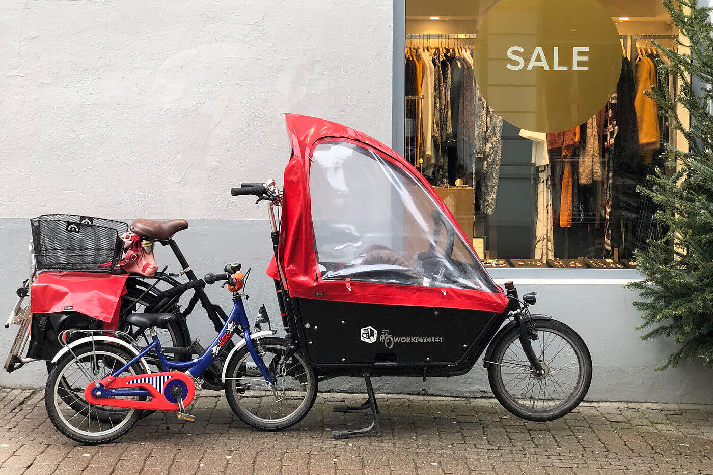 Lastenzweirad mit Babyschale in der Lastkiste und Anhängevorrichtung fürs Kinderrad